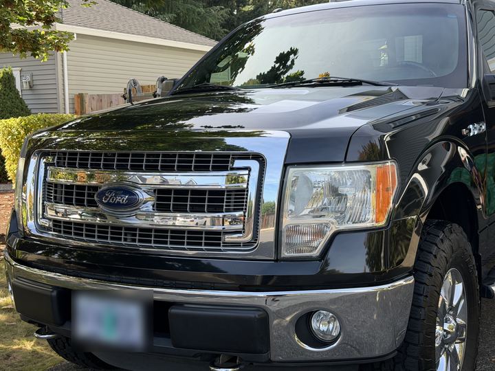 Front end of the black pickup truck after The Whole Bit, with a glossy hood, polished chrome grille, and clear headlight