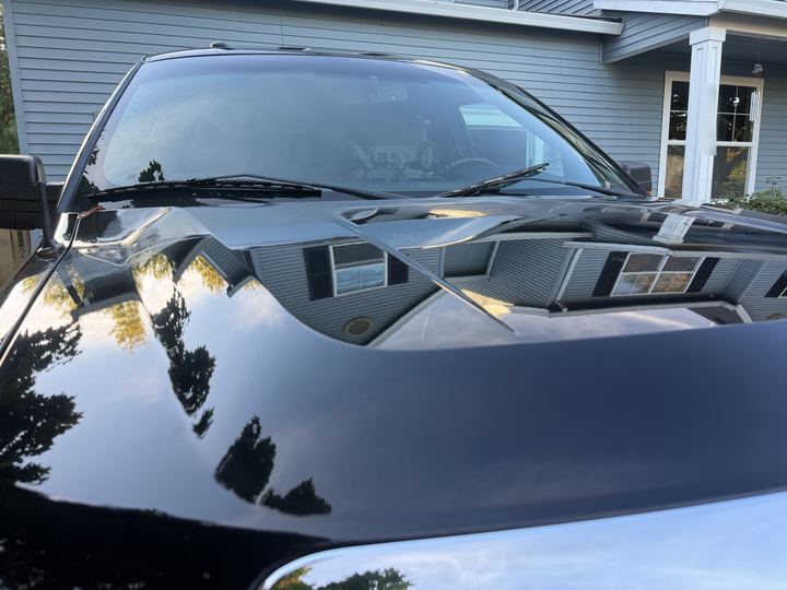 Close-up of the truck's black hood with a mirror-like reflection of the house and trees