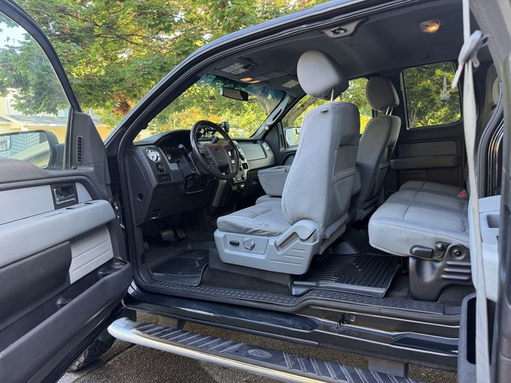 Wide view of the clean truck cab through the open doors, showing gray seats, dash, and floor mats